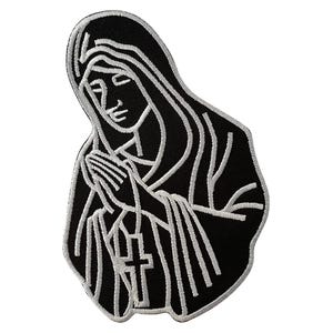 May include: An embroidered patch featuring a black background with a white line art design of a figure with a head covering and hands clasped in prayer. A rosary with a cross hangs from the hands, and the entire design is outlined in white.