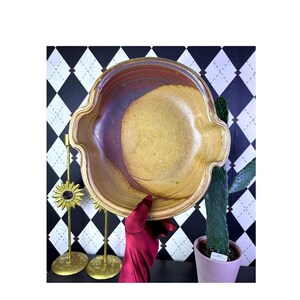 May include: A round ceramic bowl with a scalloped rim, featuring a two-tone glaze with a deep reddish-brown section and a textured, speckled golden-yellow section. The bowl has a wide, open interior and a smooth, curved edge design.