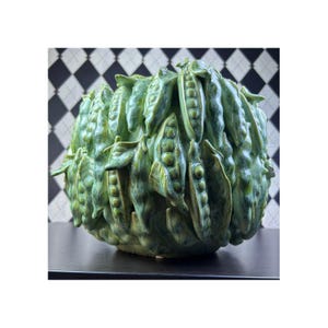 Puede incluir: Un cuenco de cerámica redondo con una superficie texturizada en tres dimensiones cubierta de vainas de guisantes verdes esculpidas. Cada vaina detalla guisantes individuales visibles, con un acabado de esmalte verde brillante y variado.