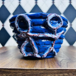 May include: A handcrafted, ceramic bowl with a vibrant blue glaze. The bowl features a textured, ribbed design with white and red accents. The unique, organic shape and color palette make it a decorative piece.