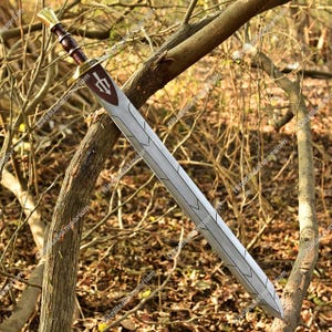 Könnte beinhalten: Ein langes, silbernes Schwert mit einem braunen Griff und einem goldfarbenen Knauf. Die Klinge hat ein dekoratives geätztes Design. Das Schwert lehnt an einem Ast und zeigt seine Länge und Details.