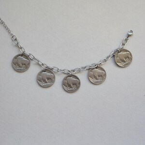 May include: A silver-toned chain bracelet featuring five circular coin charms, each displaying a relief image of an American bison and the text Five Cents. The bracelet includes a delicate link chain and a small metal lobster claw clasp closure.