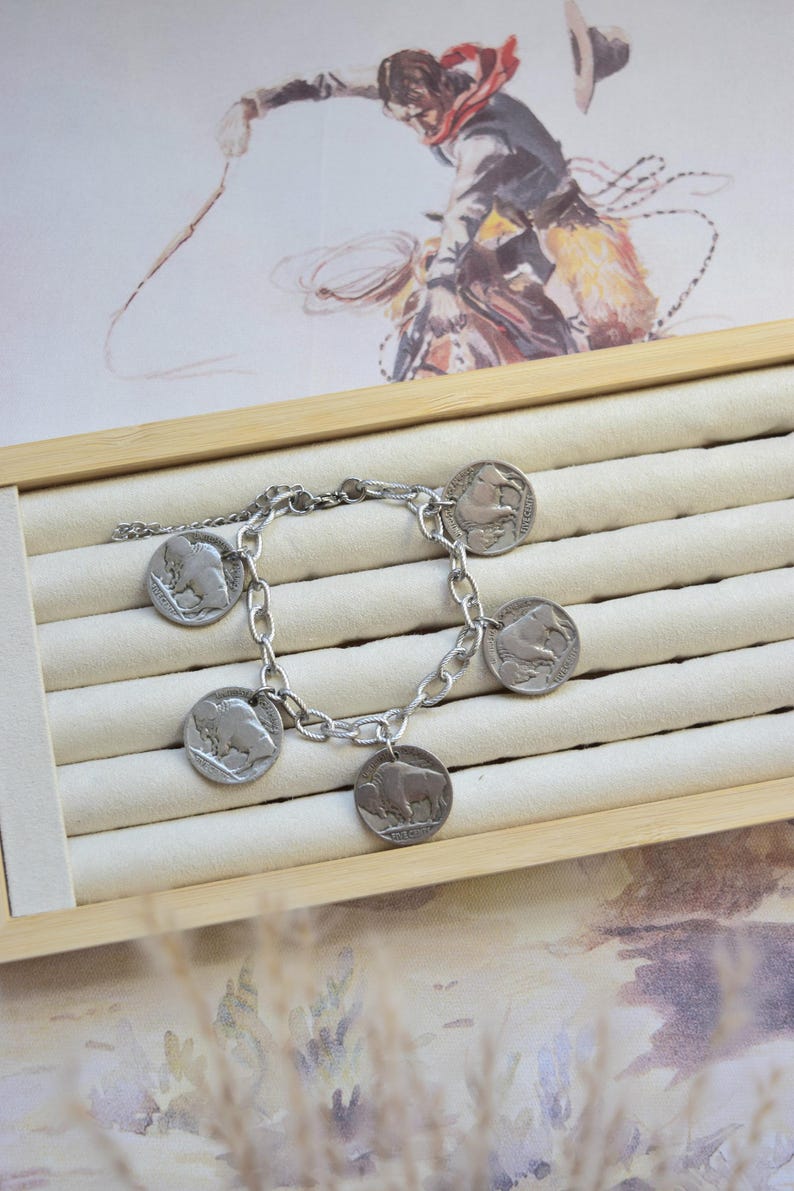 May include: A silver-toned chain link bracelet featuring five circular coin charms, each embossed with the profile of an American bison. The bracelet is constructed with a sturdy metal chain and a secure clasp, showcasing a metallic finish throughout.
