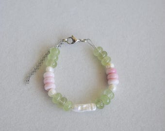 May include: A delicate bracelet featuring a mix of light green, pink, and white beads. The bracelet has a silver-colored chain and clasp. The beads are round and cylindrical, creating a unique and colorful accessory.