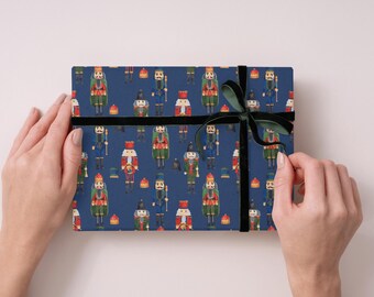 May include: A wrapped gift with a navy blue background featuring a pattern of toy nutcrackers in various uniforms. The gift is secured with a black ribbon and a dark green velvet bow.