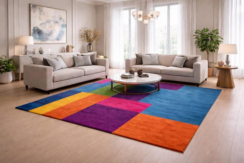 May include: A modern living room featuring two beige sofas, a round coffee table, and a colorful geometric rug. The rug has blocks of blue, orange, purple, pink, and green. The room is well-lit with natural light.