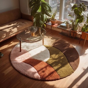 Può includere: Un tappeto circolare caratterizzato da un motivo astratto segmentato in fibre morbide e folte, con una palette di colori caldi. Il design è composto da sezioni curve e sovrapposte nei toni del rosa tenue, crema, arancio bruciato, verde oliva e marrone.