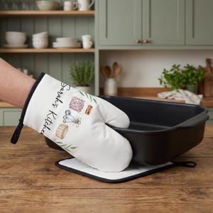 May include: A white oven mitt with black trim featuring a watercolor illustration of a jar filled with colorful sprinkles, measuring spoons, and a ramekin, with the text Sarah's Kitchen and green leaf accents printed on the front surface.