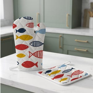 Peut inclure: Un gant de cuisine matelassé blanc et un dessous de plat carré assorti présentant un motif répétitif de poissons stylisés en rouge, bleu marine, jaune et bleu clair. Les poissons arborent des couleurs unies et des rayures sur le tissu.