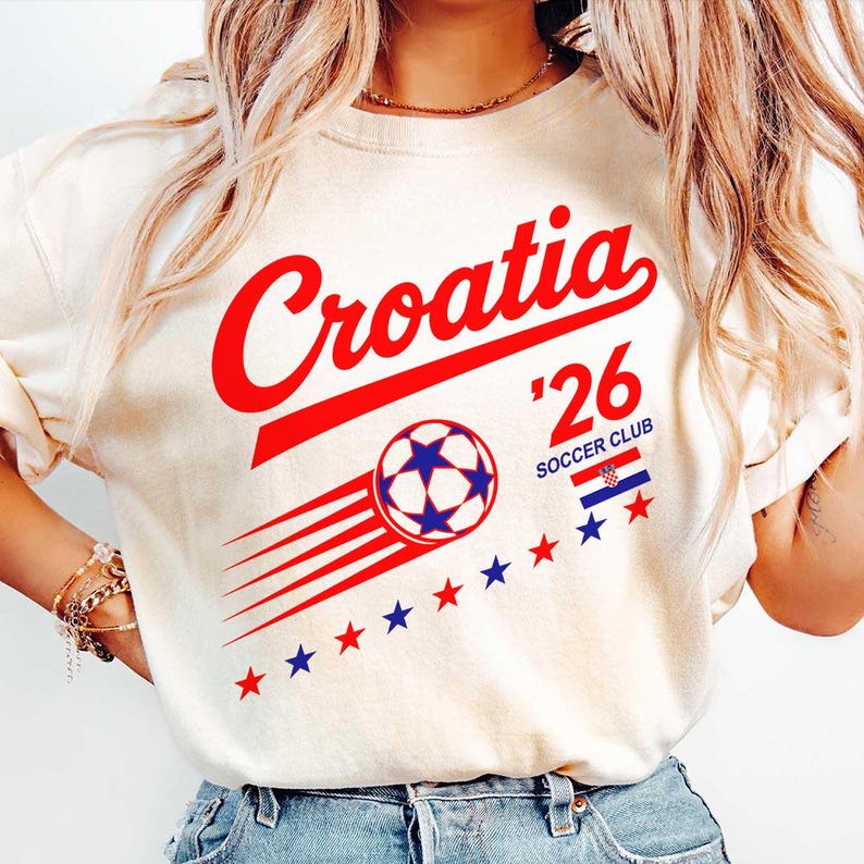 May include: A cream-colored short-sleeve t-shirt featuring the red text Croatia above a graphic of a soccer ball with motion lines. The design includes the text 26 SOCCER CLUB, a small Croatian flag, and a row of red and blue stars below the ball.