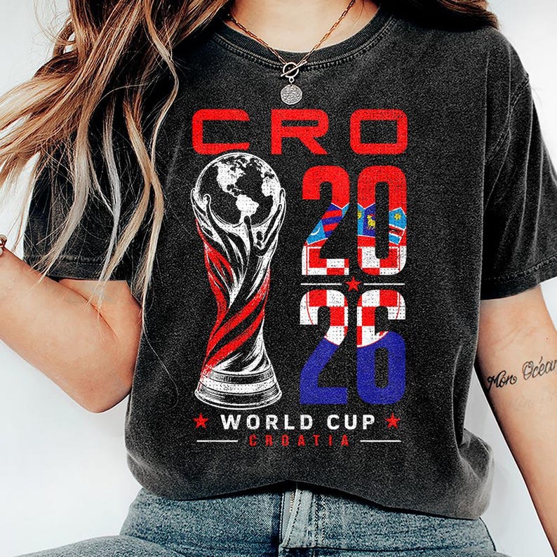 K&ouml;nnte beinhalten: Ein anthrazitfarbenes Kurzarm-T-Shirt mit einem Grafikdruck mit dem Text CRO 2026 WORLD CUP CROATIA. Das Design enth&auml;lt eine stilisierte Troph&auml;enillustration und die Zahl 2026, die mit dem rot-wei&szlig;en kroatischen Schachbrettmuster gef&uuml;llt ist.