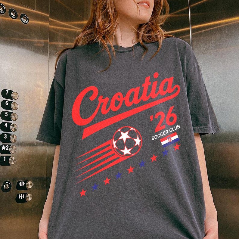 May include: A charcoal gray short-sleeve t-shirt featuring the red text Croatia, the number 26, and the words SOCCER CLUB. The graphic includes a red soccer ball with motion lines, a small Croatian flag, and a series of red and blue stars.
