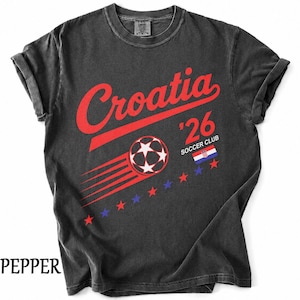 May include: A charcoal gray t-shirt featuring the red text Croatia above a graphic of a soccer ball with motion lines. The design includes the text '26 SOCCER CLUB, a small Croatian flag, and a row of alternating red and blue stars across the chest.