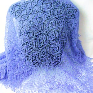 Könnte beinhalten: Ein zartes, handgestricktes Tuch in helllila. Das Tuch hat ein filigranes Spitzenmuster und einen gewellten Rand.