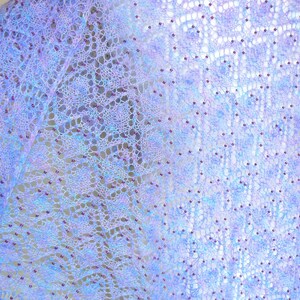 May include: A delicate, hand-knitted shawl in shades of lavender and blue with a lacy pattern and beaded accents.