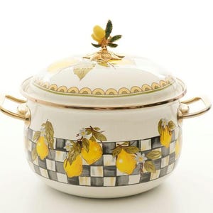 Puede incluir: Una olla de esmalte blanco con tapa, con un diseño de limones y flores. La olla tiene asas doradas y un pomo con forma de limón en la tapa. La parte inferior de la olla tiene un patrón de cuadros blancos y negros.