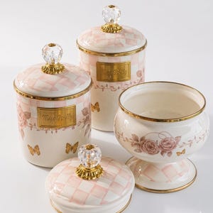 May include: A collection of four ceramic containers with a pink and white chequered design. They have gold trim, crystal knobs, and floral and butterfly patterns. The text "Miss Betty" is displayed on a gold plaque, adding a touch of elegance.
