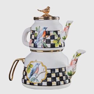May include: A white double-stacked teapot featuring a black and white checkered pattern, painted blue birds on branches, and colorful butterflies. The lid is topped with a gold-colored bird figurine, and the teapot has gold-toned metal handles.