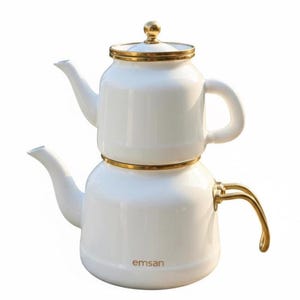 Puede incluir: Tetera de esmalte blanco con detalles dorados. La tetera tiene un diseño apilado con tapa y asa curva. El pico y el asa son dorados. La marca "emsan" está impresa en la parte inferior.