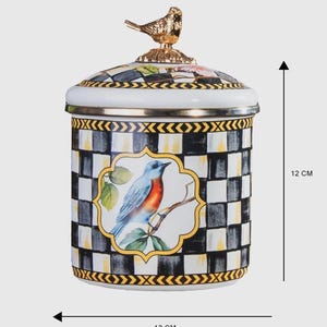 Op de afbeelding: Een decoratieve keramische pot met een deksel, met een gouden vogel als bekroning. De pot heeft een zwart-wit geblokt patroon met een omlijste afbeelding van een blauwe vogel op een tak. De pot is ongeveer 12 cm in diameter en 12 cm hoog.