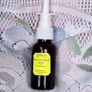 May include: A brown glass bottle with a white spray nozzle. The bottle is labeled "Mac's Pure Naturals Nasal and Mouth Spray 1% Povidone-iodine Purified Water 1% Povidone-iodine, Sea Salt"