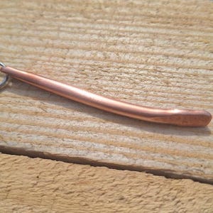 May include: A copper-coloured metal pendant shaped like a curved rod with a loop at one end.