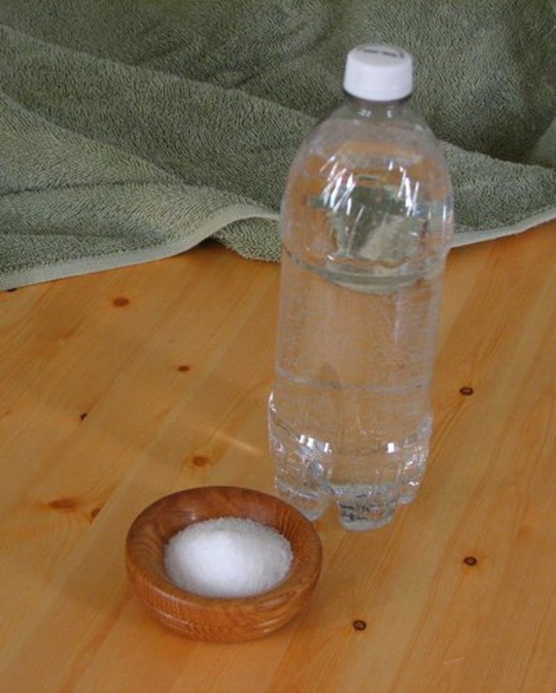 May include: A clear plastic bottle of water with a white cap, sitting on a wooden surface next to a small wooden bowl filled with white salt.