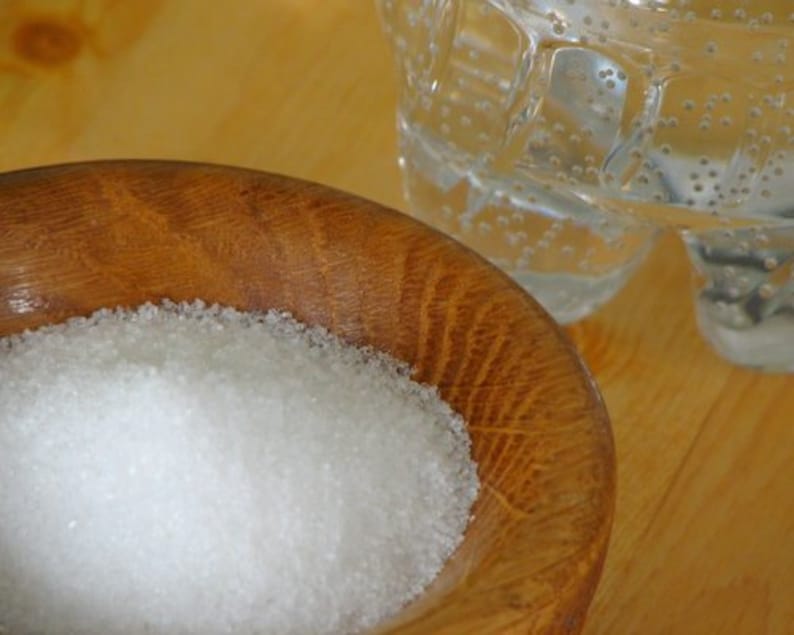 May include: A close-up of a wooden bowl filled with white granulated sugar. The bowl is sitting on a wooden surface.