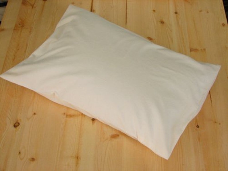 May include: A rectangular, off-white pillowcase rests on a light-colored wooden surface. The pillowcase is made of a soft, smooth fabric and appears to be empty. The pillowcase is a neutral color, suitable for various bedroom decor styles.