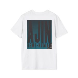 Op de afbeelding: Wit T-shirt met een grote, rechthoekige afbeelding op de rug. De afbeelding toont het woord "AJIN" in vette, donkere letters op een teal achtergrond, met "DEMI-HUMAN" eronder gedrukt in kleinere letters. Het shirt is een casual stijl.