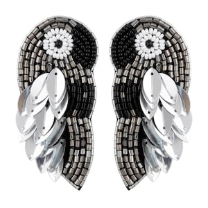 May include: A pair of statement earrings featuring a bird-shaped design crafted from black, white, and metallic gray seed beads. The earrings are embellished with silver-toned leaf-shaped sequins that create a layered, textured feather effect.