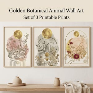 以下が含まれることがあります： 金色の植物と動物のイラストが描かれた3枚のウォールアートプリントセット。1枚目は鹿、2枚目は眠る猫、3枚目は花に囲まれた猫が描かれており、明るい木製のフレームに金色の月とアーチのモチーフが施されています。