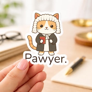 May include: A die-cut sticker featuring an orange and white cat dressed in a black judicial robe and a white barrister wig. The cat holds a small red book, and the text below reads Pawyer. The sticker has a white border.