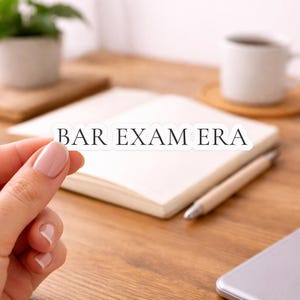 May include: A die-cut sticker featuring the text BAR EXAM ERA in a bold, black, serif font. The sticker has a clean white border around the lettering, creating a clear and legible design for application on various smooth surfaces.