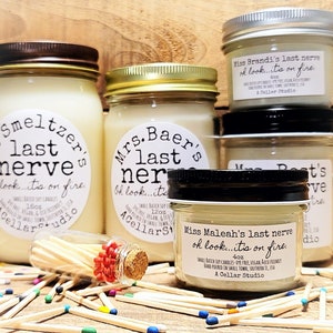 May include: Four glass jars with white candles and black labels. The labels have the text "last nerve" and "oh look...it's on fire". The jars are surrounded by a pile of colorful matchsticks.