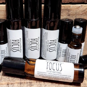 May include: A close-up of multiple 10 ml amber glass roller bottles with black caps and silver roller balls. The bottles are labeled "FOCUS 100% NATURAL" and list ingredients including sweet almond and grapeseed oils, pink grapefruit, black pepper, lime, lavender, spearmint, and essential oils.