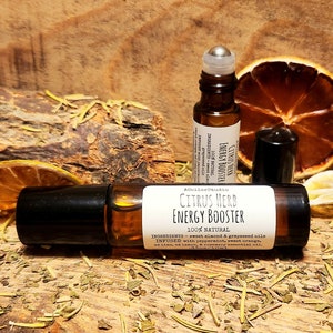 May include: A clear glass roller bottle with a black cap and label that reads "Citrus Herb Energy Booster 100% Natural" with ingredients listed below. The bottle is sitting on a wooden surface with dried citrus fruit and herbs.
