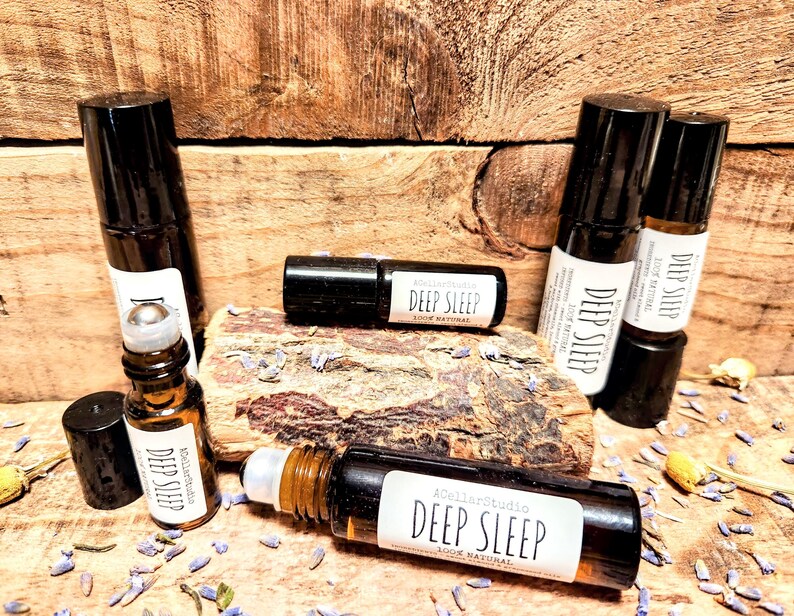 May include: Five brown glass roller bottles with black caps and labels that say "Deep Sleep 100% Natural". The bottles are arranged on a wooden surface with dried lavender flowers.