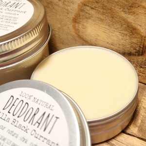 Puede incluir: Una lata de plata con una etiqueta blanca que dice "100% NATURAL DESODORANTE Vainilla Grosella Negra". La lata est&aacute; llena de una crema de color amarillo claro.