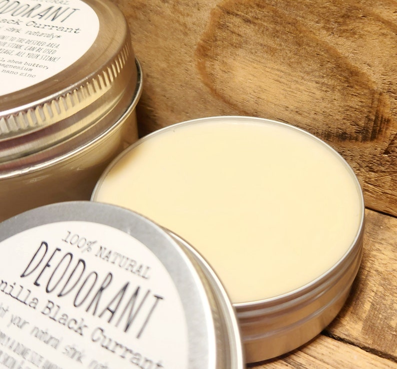 Puede incluir: Una lata de plata con una etiqueta blanca que dice "100% NATURAL DESODORANTE Vainilla Grosella Negra". La lata est&aacute; llena de una crema de color amarillo claro.