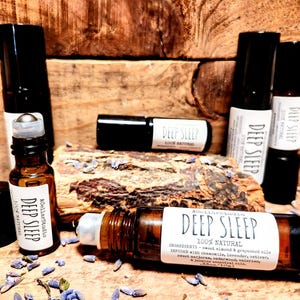 May include: A collection of amber glass roller bottles with black caps and labels that read "Deep Sleep 100% Natural". The bottles are arranged on a wooden surface with dried lavender flowers.