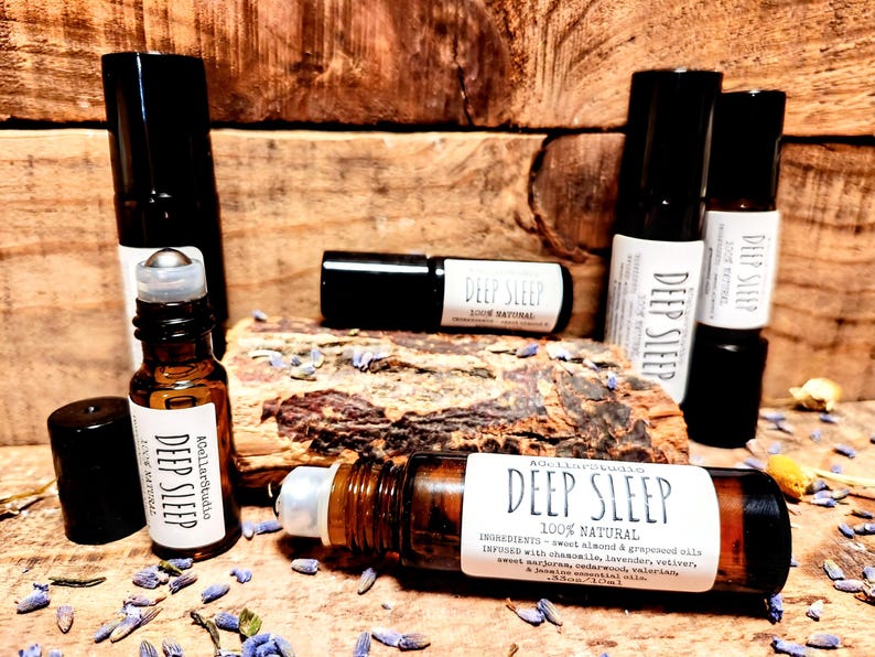 May include: A collection of amber glass roller bottles with black caps and labels that read "Deep Sleep 100% Natural". The bottles are arranged on a wooden surface with dried lavender flowers.