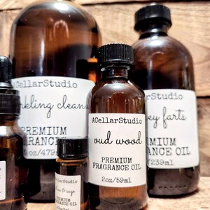 May include: Five amber glass bottles with black lids containing premium fragrance oil. The bottles are labeled with the brand name "ACellarStudio" and the fragrance names "Oud Wood", "Honey Farts", "Teak & Sage", "Clinking Clean", and "Premium Ranch". The bottles are arranged on a wooden surface.