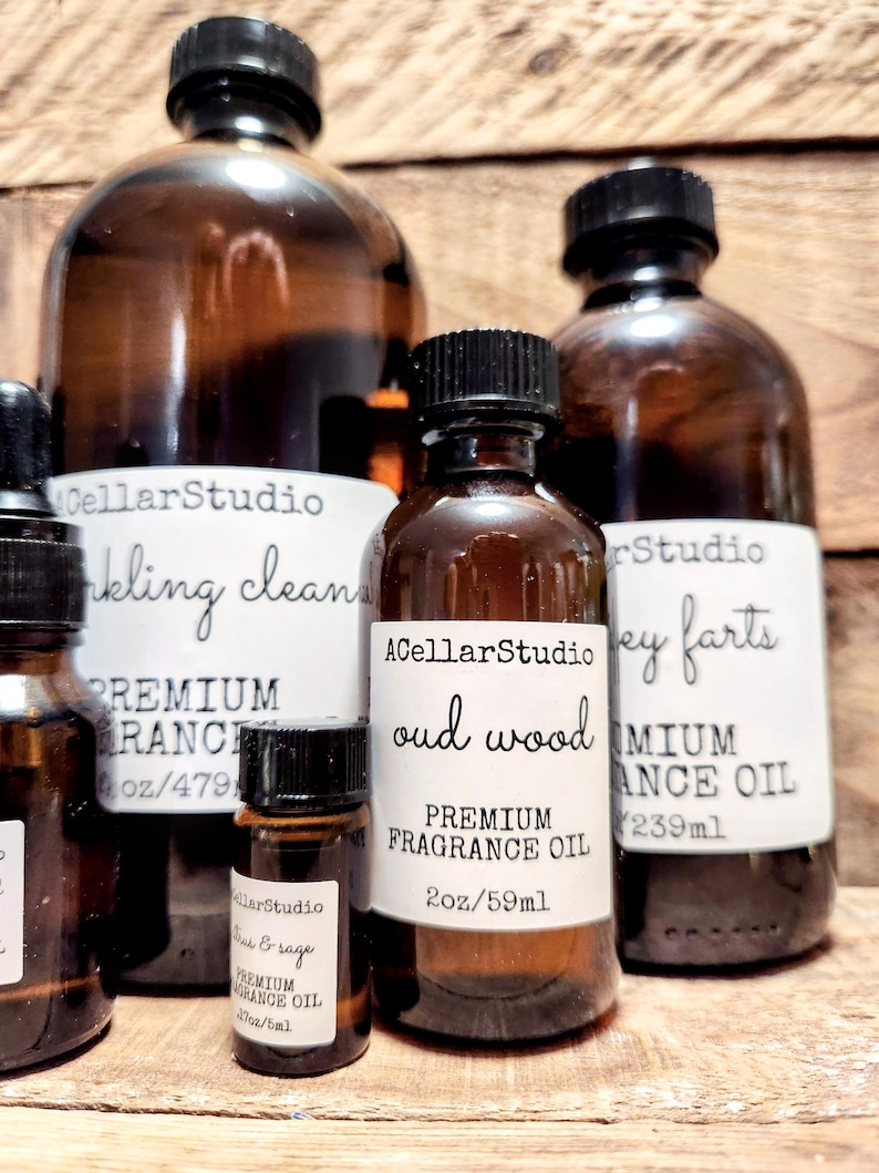 May include: Five amber glass bottles with black lids containing premium fragrance oil. The bottles are labeled with the brand name "ACellarStudio" and the fragrance names "Oud Wood", "Honey Farts", "Teak & Sage", "Clinking Clean", and "Premium Ranch". The bottles are arranged on a wooden surface.