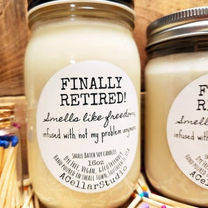 K&ouml;nnte beinhalten: Eine wei&szlig;e Sojawachskerze in einem Glasgef&auml;&szlig; mit schwarzem Deckel. Das Etikett lautet "FINALLY RETIRED! Smells like freedom infused with not my problem anymore" und "SMALL BATCH SOY CANDLES 16oz DYE FREE. VEGAN. & ECO FRIENDLY HAND POURED IN SMALL TOWN. SOUTHERN IL USA ACellarStudio".