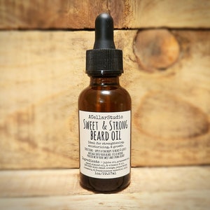 May include: A brown glass bottle with a black dropper top and a white label that reads "ACellarStudio Sweet & Strong Beard Oil Ideal for strengthening, moisturizing, & growth. Directions: Apply a few drops to beard & gently massage into your beard. Just a few drops produce a soft, smooth, and strong beard. Ingredients - Jojoba oil, grapeseed oil, sweet almond oil, & vitamin E oil. Infused with sweet orange essential oil, rosemary, & frankincense essential oils. 1oz/29.57ml"