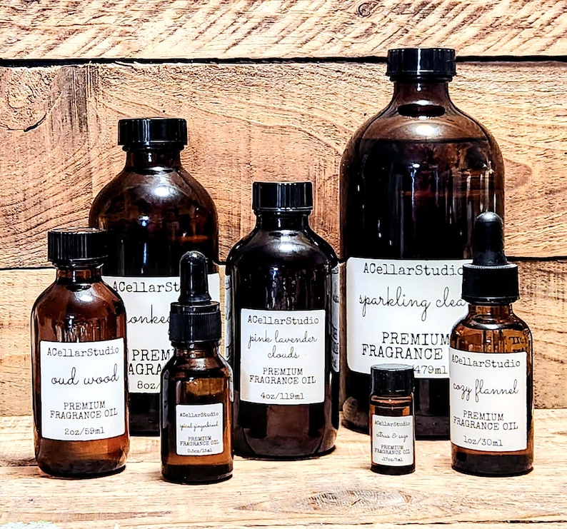 May include: A collection of amber glass bottles with droppers, containing premium fragrance oils. The bottles are labeled with names like "oud wood", "pink lavender clouds", "sparkling clean", and "cozy flannel". Each bottle has a label with the text "ACellarStudio" and "Premium Fragrance Oil".