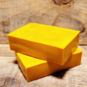 May include: Two bars of bright yellow soap stacked on top of each other. The soap is on a wooden surface.