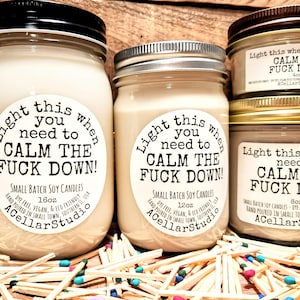 May include: Several soy candles in glass jars with metal lids. The labels read "Light this when you need to CALM THE FUCK DOWN!". Sizes include 16oz, 12oz, 8oz, and 4oz. The candles are surrounded by matches.