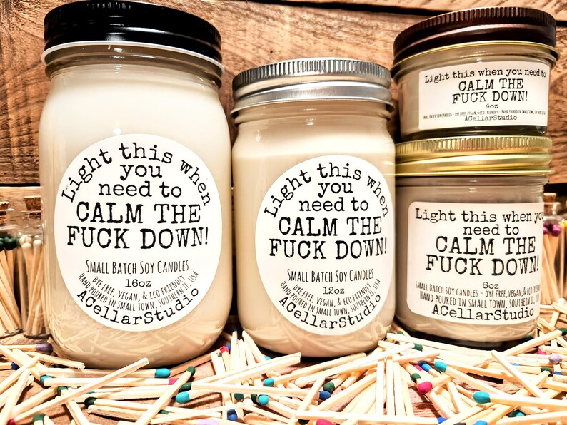May include: Several soy candles in glass jars with metal lids. The labels read "Light this when you need to CALM THE FUCK DOWN!". Sizes include 16oz, 12oz, 8oz, and 4oz. The candles are surrounded by matches.
